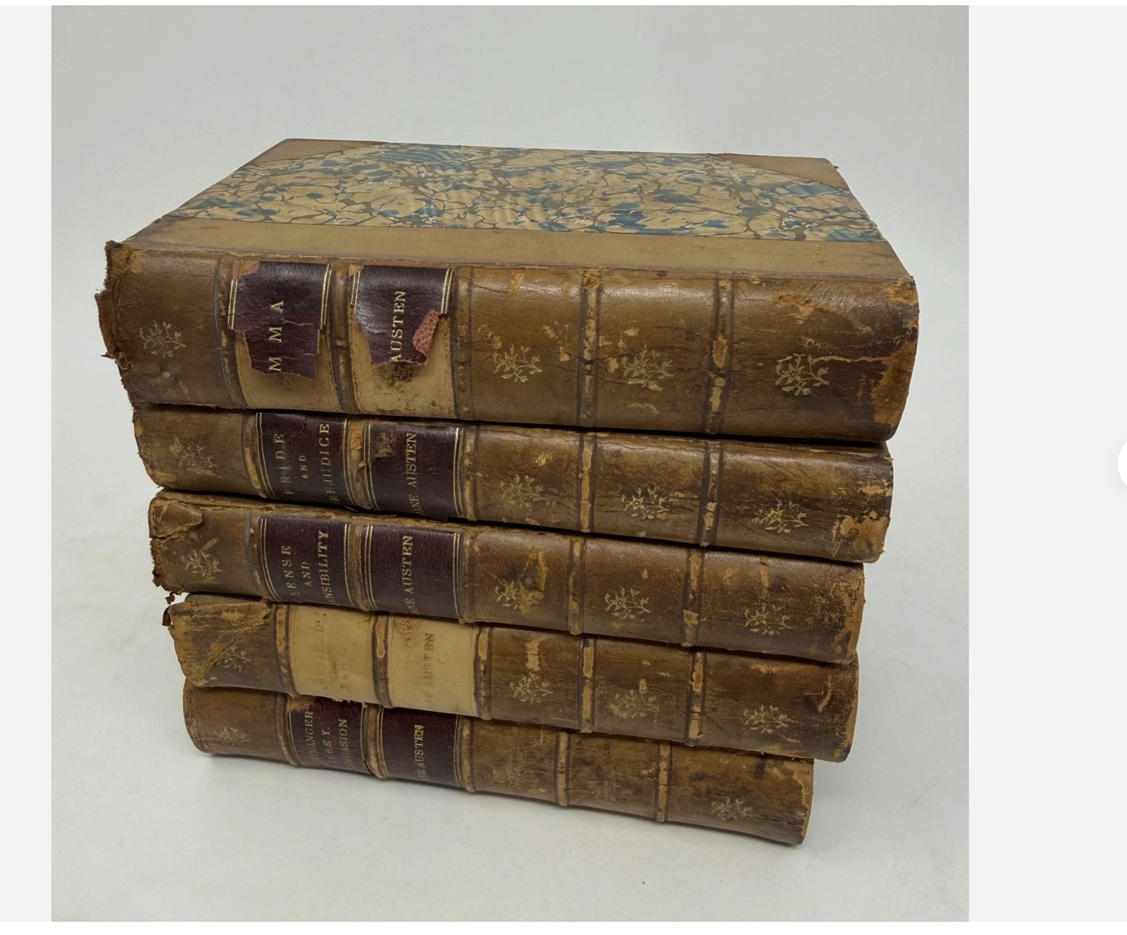 Stack of five antique leather-bound Jane Austen volumes — Emma, Pride and Prejudice, Sense and Sensibility — with worn marbled boards and gilt spine labels, the kind of genuine antiquarian set that holds real value.